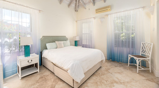 Carlton Ridge guest bedroom with graduated blue voile curtains and turquoise lamps under vaulted beams, Barbados