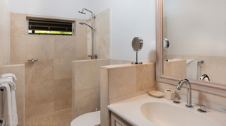 Travertine-tiled bathroom with a walk-in rain shower and pale-wood mirror at Church Point 2 villa, Barbados
