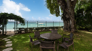 Garden dining table under a shade tree with the Caribbean Sea beyond the gate at Church Point 2, Barbados