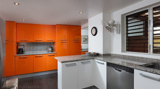 Galley kitchen with glossy orange cabinets and granite worktops at Church Point 2 villa, Barbados