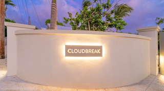 Backlit Cloudbreak nameplate glowing on its curved entrance wall against a violet dusk sky, Barbados