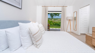 Bedroom opening to a terrace and countryside views past a pale upholstered bed at Cloudbreak, St. James, Barbados