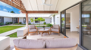 Teak armchairs on a bedroom's covered terrace beside sliding doors to the garden at Cloudbreak villa in Barbados
