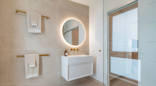 Round backlit mirror, brass mixer and brass towel rails in a stone-tiled bathroom at Cloudbreak, Barbados