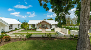 Garden elevation of Cloudbreak framed by a shade tree, its gabled terrace open between white-roofed wings, Barbados