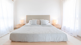 Bedroom with a tall beige upholstered headboard and twin lamps between sheer-curtained windows at Cloudbreak, Barbados