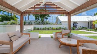 Covered terrace with teak seating opening onto the enclosed garden lawn at Cloudbreak villa in Barbados