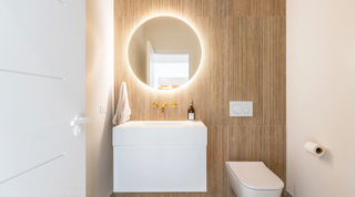 Powder room with a fluted timber feature wall, backlit mirror and brass mixer at Cloudbreak villa, Barbados