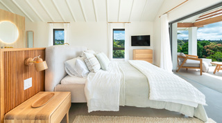Grey upholstered bed with a wall TV and fluted-timber bedside panel opening to countryside at Cloudbreak villa, Barbados