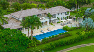 Long infinity pool edged by flowering hedges, with silver fan palms and the Apes Hill golf course below Cocomaya, Barbados