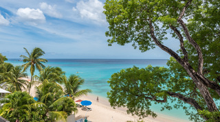 View over palm tops to the beach, with a jet ski and yachts beyond, at Coral Cove 14 – Crowsnest in St. James, Barbados