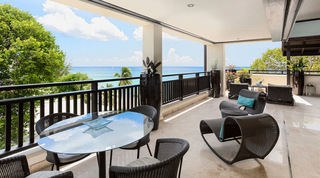 Covered terrace at Coral Cove 14 – Crowsnest in Barbados, with a round glass table and wicker rocking lounger facing the sea