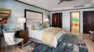 Desk and acrylic chair by the bed at Coral Cove 14 – Crowsnest in Barbados, with the walk-in wardrobe and en suite beyond