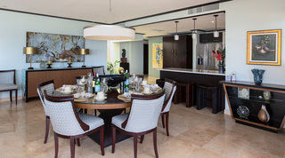Round dining table laid with cream china under a drum pendant, breakfast bar beyond, at Coral Cove 14 – Crowsnest in Barbados
