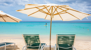 Paddleboarder and child glimpsed between two parasol-shaded loungers, Coral Cove 14 – Crowsnest beach apartment in Barbados