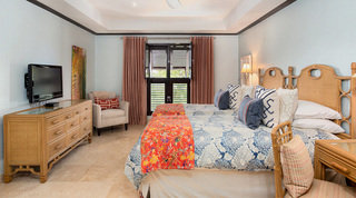Twin bedroom at Coral Cove 14 – Crowsnest in Barbados, with a cane-panelled chest of drawers, television and cream armchair