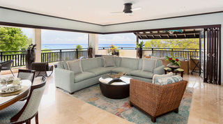 Living room at Coral Cove 14 – Crowsnest in Barbados, with a grey-green L-shaped sofa, woven armchair and abstract rug