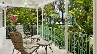 Wicker chairs on a verandah looking past palms to the pool and sea, Crystal Springs, St. James, Barbados