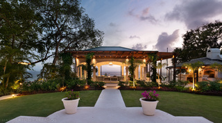 Vine-clad garden loggia lit above the sea at dusk, with lawn and flowering urns, Crystal Springs, Barbados