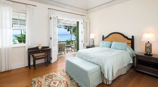 Aqua bedroom with a cane headboard and writing desk opening to a sea-view terrace at Four Winds, Barbados