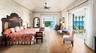 Master bedroom with a carved wood bed and doors to a sea-view terrace at Four Winds luxury villa, Barbados