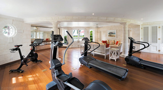 Air-conditioned gym with treadmills and a cross-trainer on a wood floor at Four Winds, Barbados