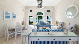 Striped blue and white sofas in a coral-stone sitting room open to the sea at Four Winds, a holiday villa in Barbados