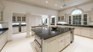 Twin stone columns, a coffee station and a polished granite island in the kitchen at Four Winds, Barbados holiday villa