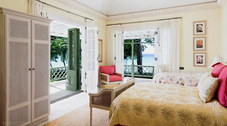 Yellow bedroom with a cane wardrobe and French doors to a sea-view balcony at Four Winds, Barbados