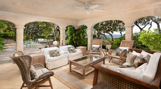 Arched loggia at Fustic House with cane-backed lounge chairs, white armchairs and a glimpse of the sea, St. Lucy, Barbados