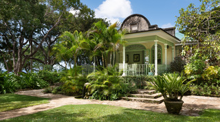 Sculpted fountain and palms before a curved-gable veranda with green trim in the Fustic House gardens, Barbados