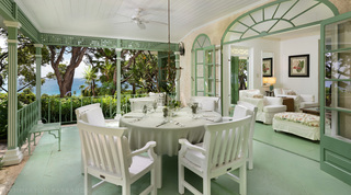 Round veranda table with white chairs framed by sea views through the trees at Fustic House in Barbados