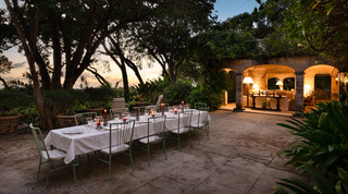 Candlelit dinner table on the terrace at sunset beside the lamp-lit arched loggia of Fustic House, Barbados