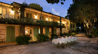 Evening at Fustic House in Barbados, the Great House lit behind a candlelit table set on the terrace