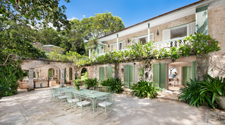 Sunlit courtyard with a green metal table and chairs in front of the vine-hung Great House, Fustic House in Barbados