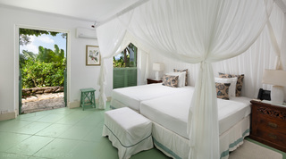 Twin beds under a sheer white canopy, green louvred shutters and a door to the garden at Fustic House, Barbados