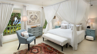 Bedroom at Fustic House with a sheer-canopied bed, pale blue armchair and a sea-view balcony, Barbados