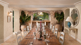 Painted monkey mural in a brick-arched stone wall beyond the laid dining table and terracotta urns, Fustic House, Barbados