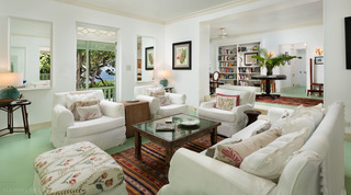 Sitting room with white slipcovered armchairs, a botanical print and bookshelves beyond, Fustic House in Barbados
