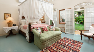 In a Fustic House suite, a carved wooden bed, green sofa and kilim rug by French doors to the lawn, Barbados