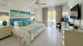 King bed with a blue painted plank headboard beneath a beach triptych, Glitter Bay 107 holiday apartment, Barbados