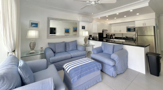 White gloss kitchen and breakfast bar opening onto the blue living room seating at Glitter Bay 107, apartment in Barbados