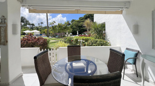 Glass dining table and wicker chairs on the covered terrace, with gardens and the pool beyond, Glitter Bay 107, Barbados