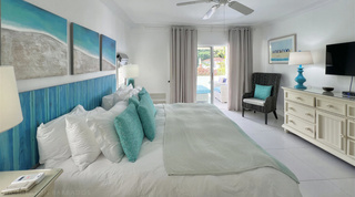 Principal bedroom with a beach-hut print and wicker armchair by the terrace door of Glitter Bay 107 in Barbados