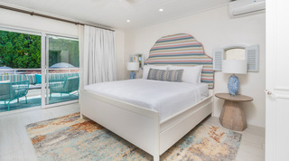 Glitter Bay 204 Sea Men's Inn king bedroom with a multicolour striped headboard and terrace doors, Barbados apartment