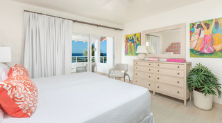 Glitter Bay 301 – The Lighthouse king bedroom with pale dresser and figurative art opening to a balcony, Barbados