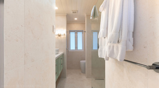Stone-clad bathroom with walk-in shower and robes on the rail at Glitter Bay 301 – The Lighthouse, Barbados