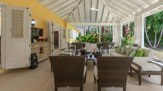 Covered terrace lounge under a vaulted ceiling opening to the garden at Jamoon villa in Barbados