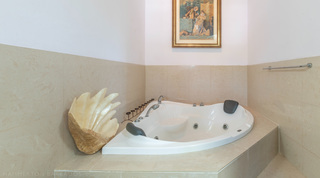Corner whirlpool bath with a shell ornament and tiled surround at Jamoon villa, Barbados