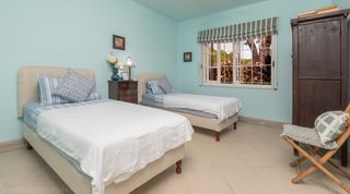 Turquoise twin bedroom with two singles and a dark armoire at Jamoon, Barbados